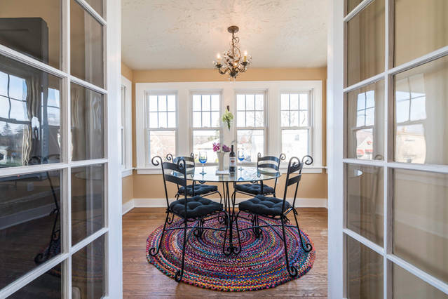 A sunroom with a colorful round rug and a round glass table with chairs and a small chandelier