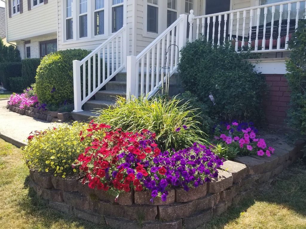 A colorful front yard flower garden area with white porch rails leading to the front door