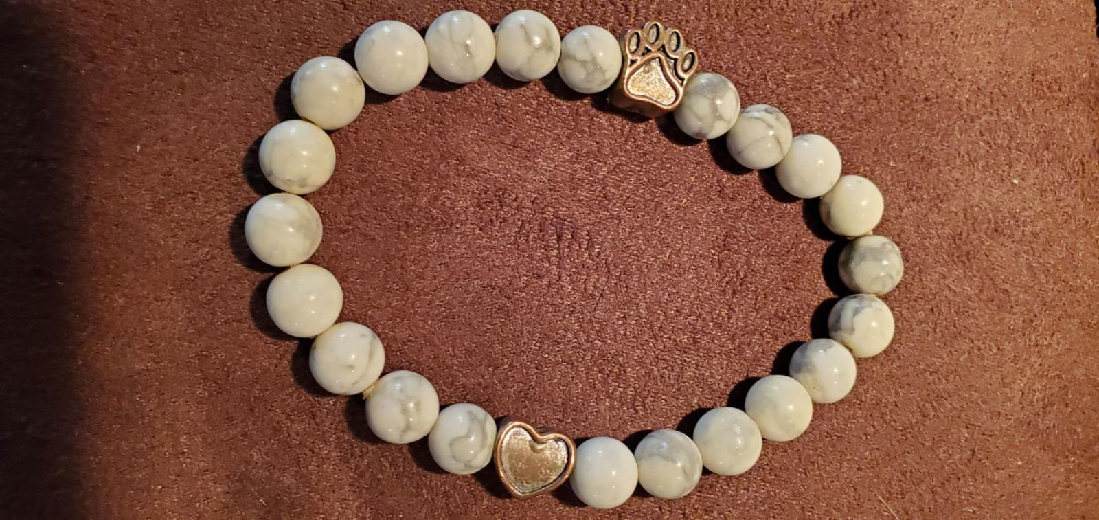 A moonstone elastic bracelet with a paw print and heart charm. The moonstone is a light grey and creamy white color.