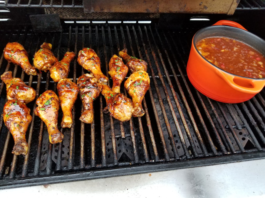 Char broiled chicken legs or drumsticks with beautiful golden grill marks. Also an orange bast iron crock pot filled with homemade pork and beans.