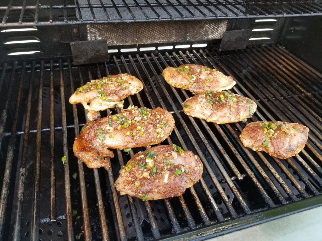 Raw marinaded chicken breast on a grill. marinated with garlic and green onion pieces.