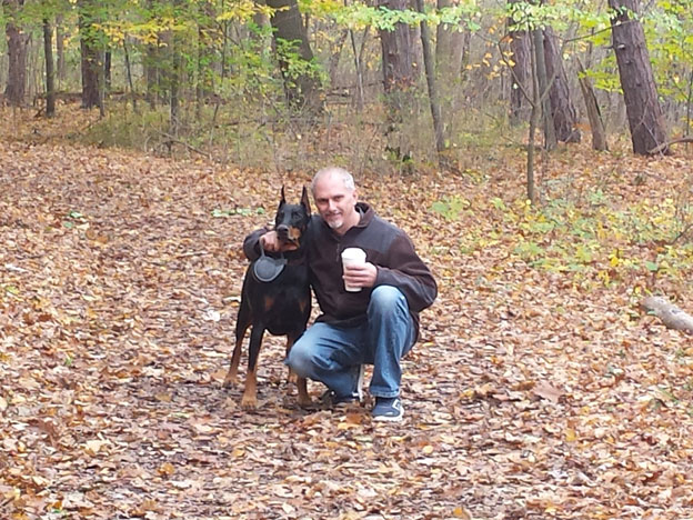 A man and a doberman in the park with beautiful fall leaves