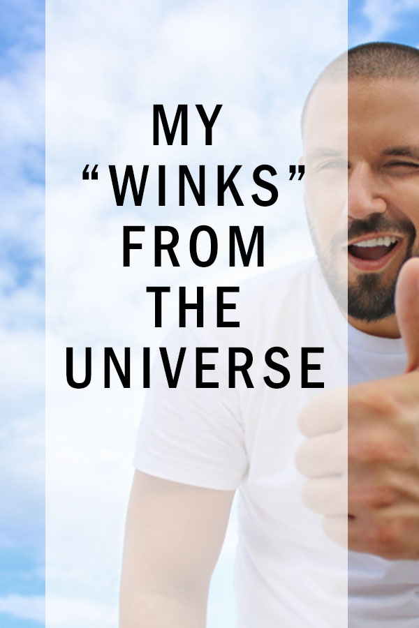 A blue sky background with clouds and a handsome man with a nicely trimmed head and mustache and beard in a white T-shirt. Giving the thumbs up. Title in white shaded transparent box says My Winks From The Universe.