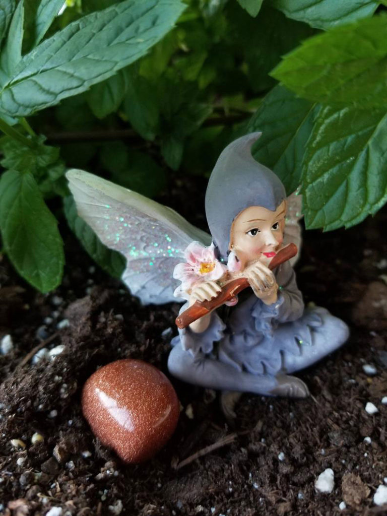 A piece of glittery goldstone with a lavender color pixie playing a flute