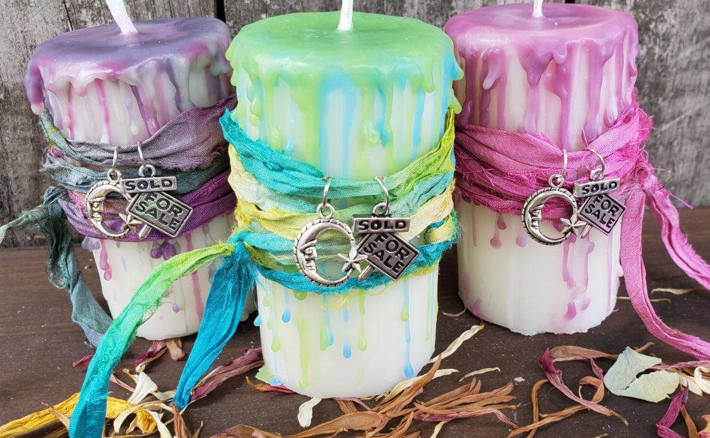 Photo of 3 handmade Reiki charged white pillar candles with green, purple and fuschia color drip wax and ribbons. Each candle has two charms. One of a moon and one of a For Sale/sold sign
