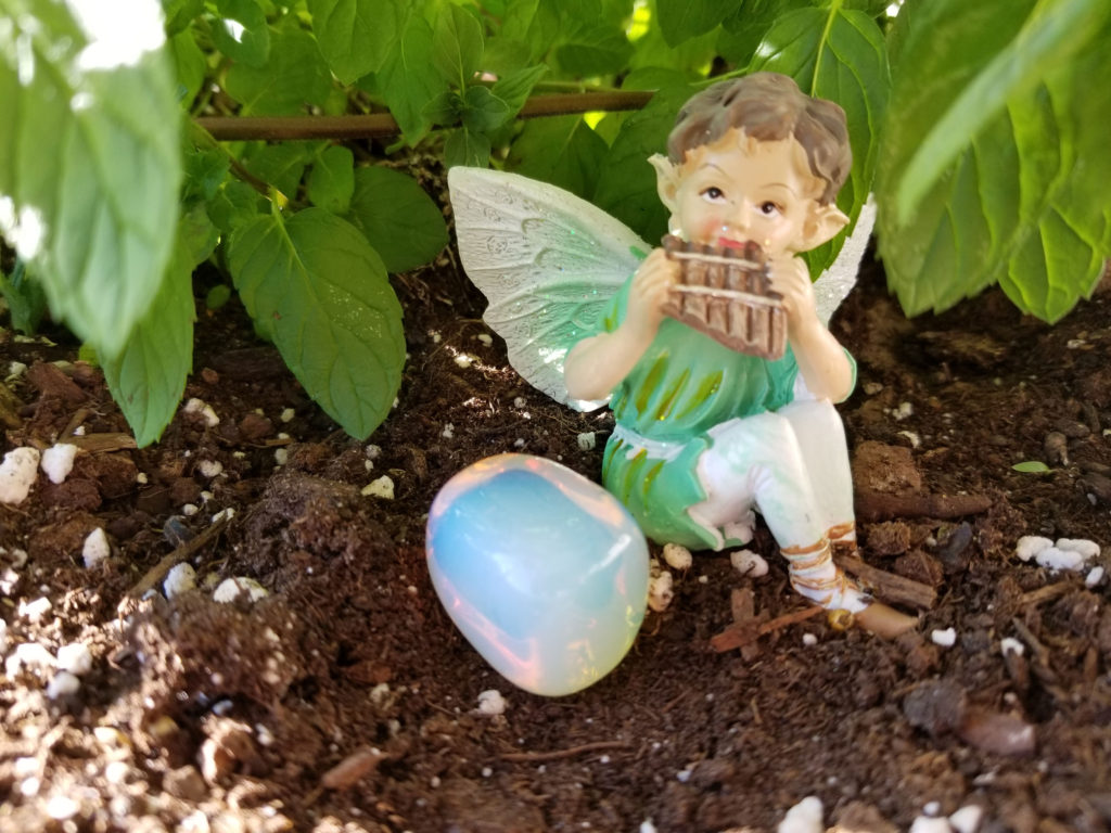 A piece of iridescent Opalite with a little boy Pixie playing a flute dressed in light green with wings