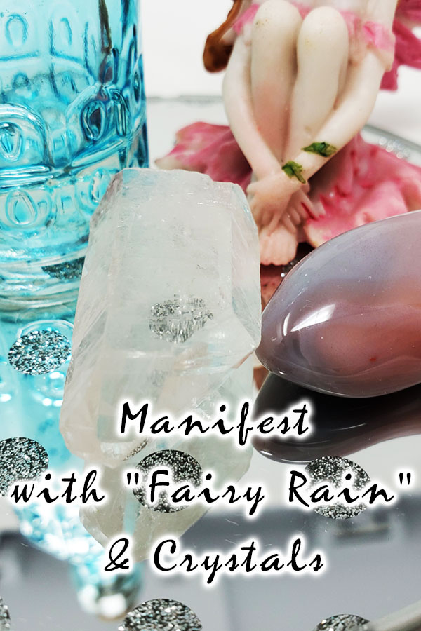 A clear quartz crystal and Botswana crystal sitting on a mirror with a blue bottle and pink sitting fairy with the words manifest with fairy rain and crystals