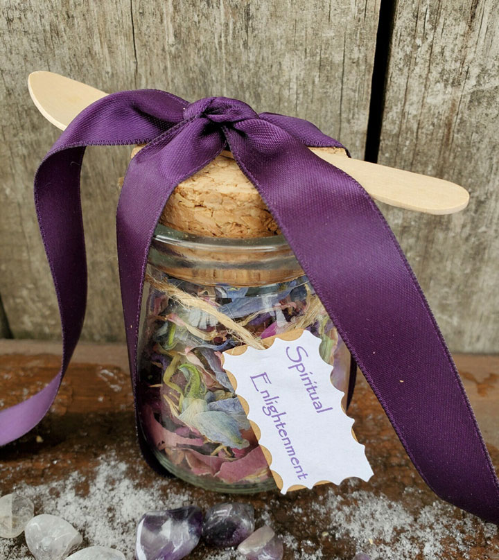 A jar with a wooden spoon and a purple satin ribbon tied around it. Filled with hand blended dried flowers and herbs with a label "Spiritual Enlightenment"