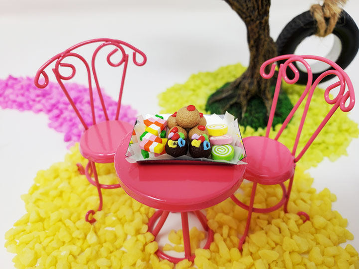 A bubble gum pink fairy bistro table and two chairs. A colorful dessert tray sits on top of the table with lots of sweet goodies