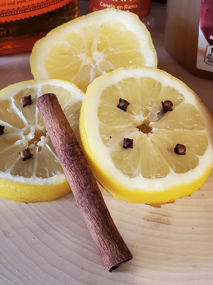 A photo of 3 lemon slices with a cinnamon stick and 4 whole cloves stuck in each lemon slice