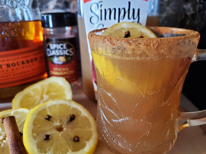 A Hot Toddy drink. A cinnamon rimmed clear mug with a lemon wedge and cloves