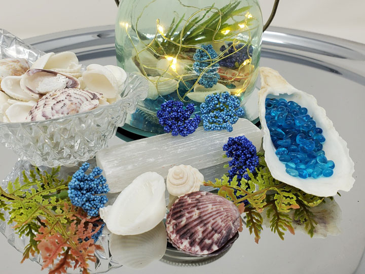seashells, a selenite crystal wand, water beads in a clam shell artificial foliage and a lighted glass jar