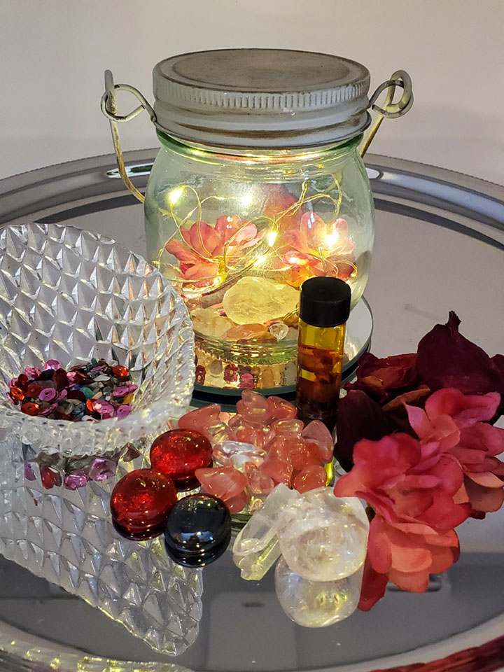 Clear Quartz crystals a glass bowl of sequins and resins, artificial pink and red flowers, spell oil and a lighted glass jar