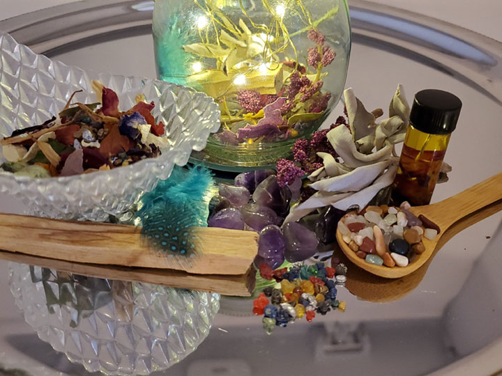 A palo santo stick, colorful resins, crystal ships, white sage, Amethyst crystals, dried herbs, a bottle of spell oil and a lighted glass jar kit
